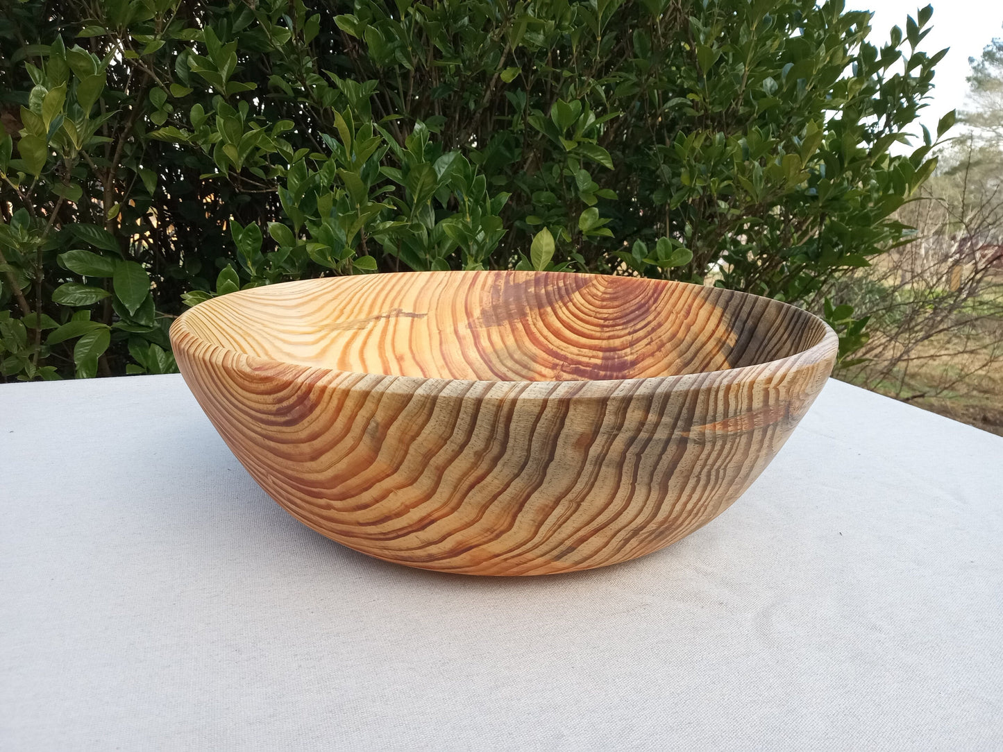 a wildly figured round pine wood bowl with streaks of resin extending out from the heart in the sidewall. Bluish black tones contrast with the vibrant orange hues of the resin pockets. The bowl is set on a white table cloth