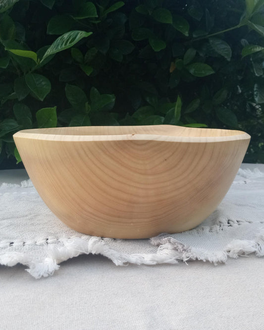 a light wood bowl with a naturally wavy edge and accentuated growth rings in the sidewall sitting on a woven cotton table runner.