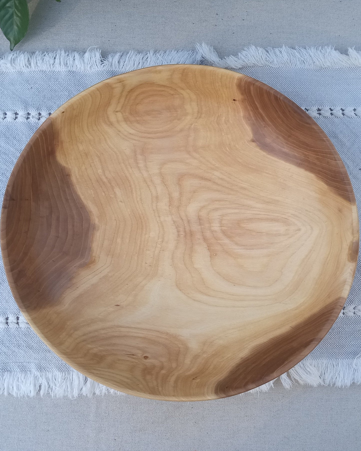 top view of a shallow figured elm wood bowl with three deep amber colored spots on the sides and pale cream in the middle set on a pale blue woven cotton table runner