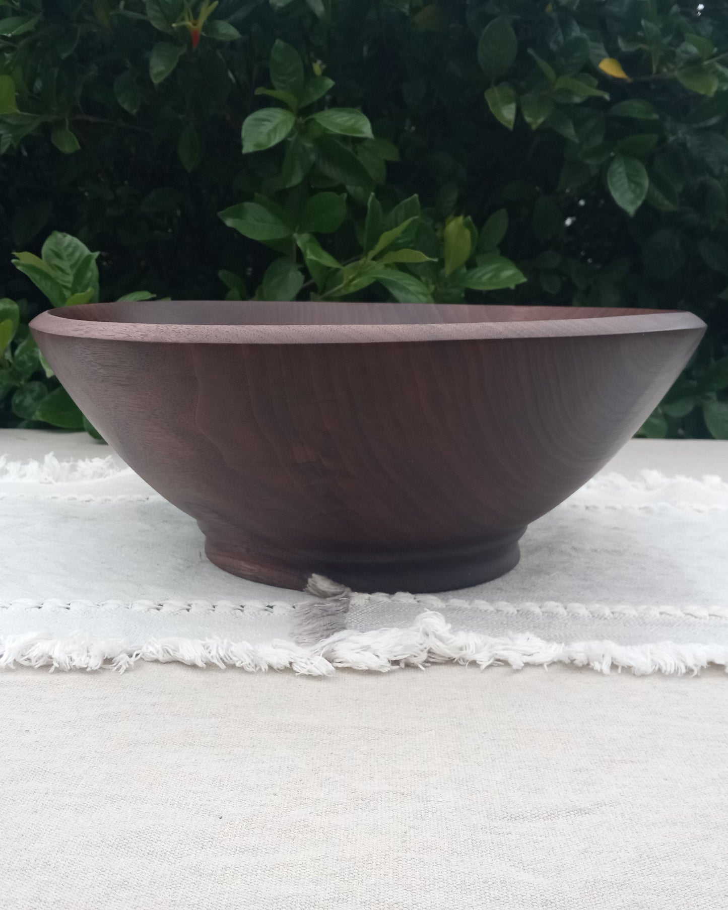 a wide dark wood bowl with a finely carved edge, tapered sides and   exquisitely carved footing set on a pale gray cotton table runner