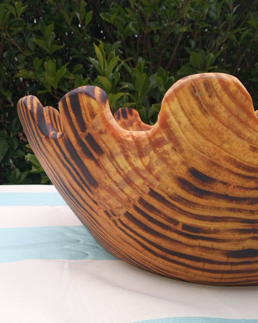 close up of a deep round wood bowl torched to create black stripes that accentuate the grain of the wood. The rim is carved into continuous wavy S shapes that could function as slots for the salad spoons