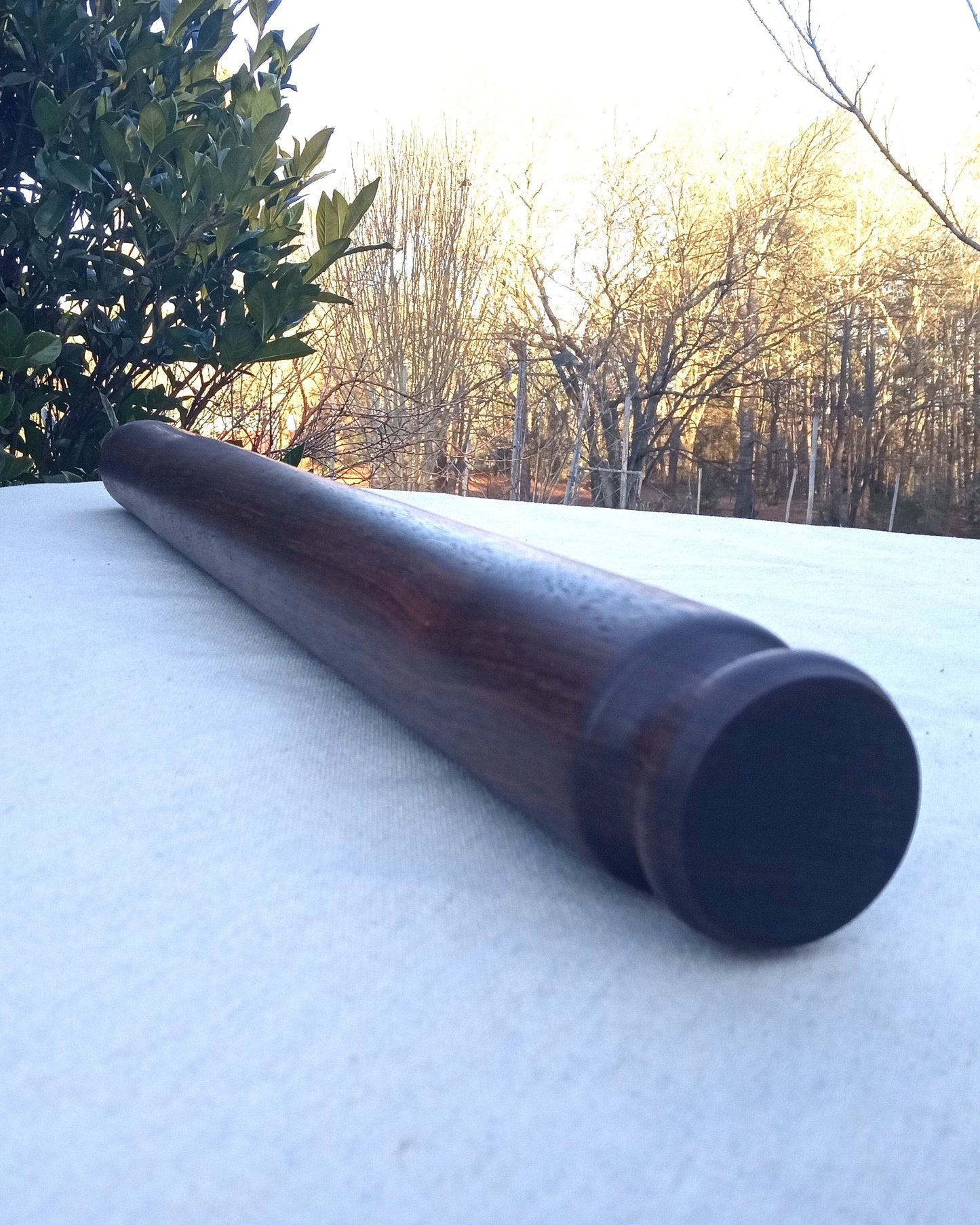 A long walnut wood rolling pin with a fancy decorative end sitting on a white table cloth.